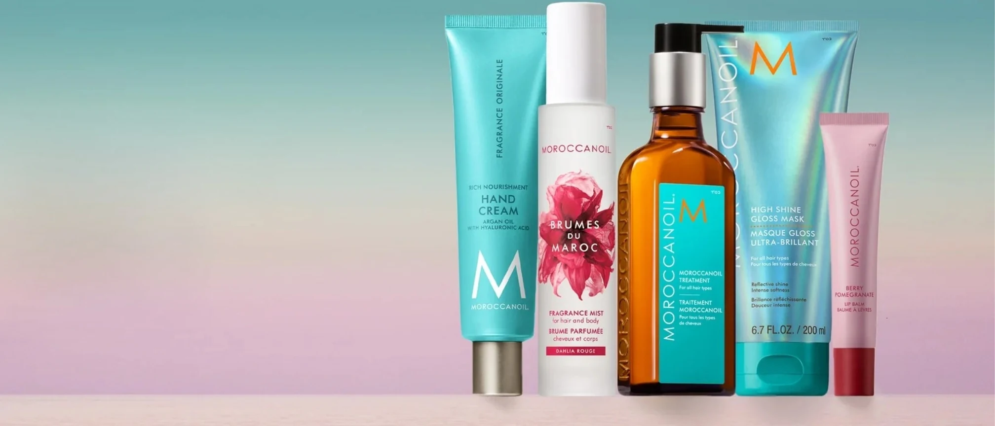Moroccanoil Sortiment: Treatment-&Ouml;l, Hand Cream, Fragrance Mist, Gloss Mask und Lippenpflege vor pastellfarbenem Verlauf